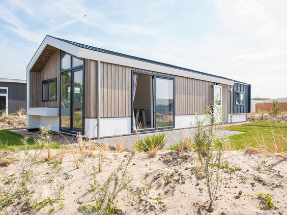 Een moderne en duurzame familielodge met grote ramen, gelegen in een open zandlandschap op vakantiepark De Wije Werelt op de Veluwe.