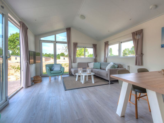 Lichte woonkamer van een moderne lodge op De Wije Werelt, met een comfortabele zithoek, eettafel en grote ramen met uitzicht.