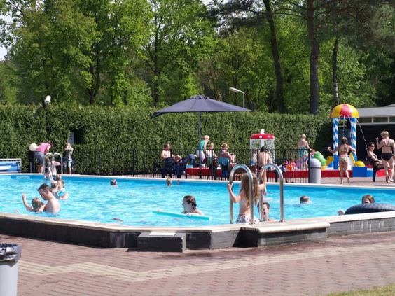 Het verwarmde buitenzwembad van De Wije Werelt, met spelende kinderen in het water en een aparte waterspeeltuin voor de kleintjes.