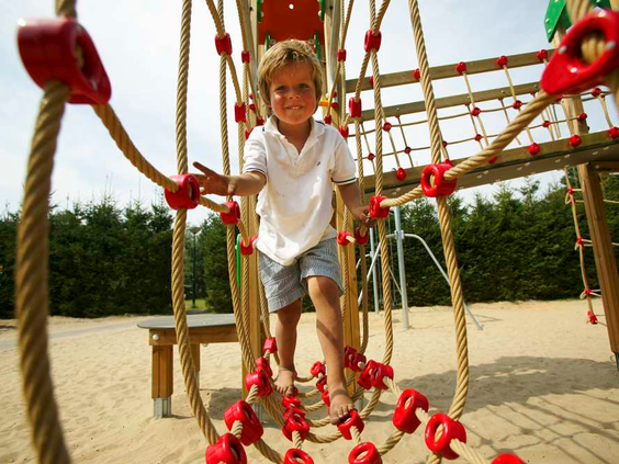 Een jongen balanceert op een touwbrug in de avontuurlijke buitenspeeltuin met zand bij kindvriendelijk vakantiepark De Wije Werelt.