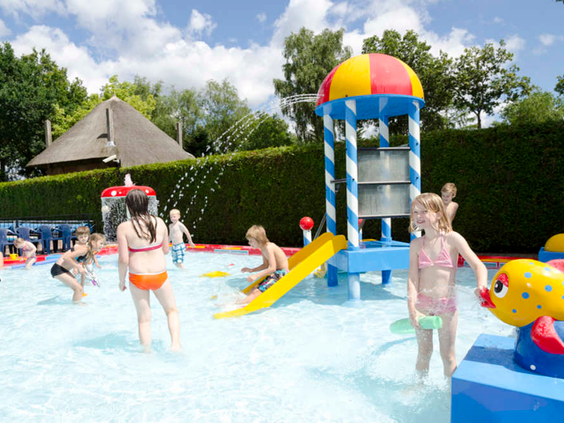 Kinderen spelen en spetteren in de waterspeeltuin 't Houtse Hoofd bij De Wije Werelt, met een glijbaan en watersproeiers voor waterpret.