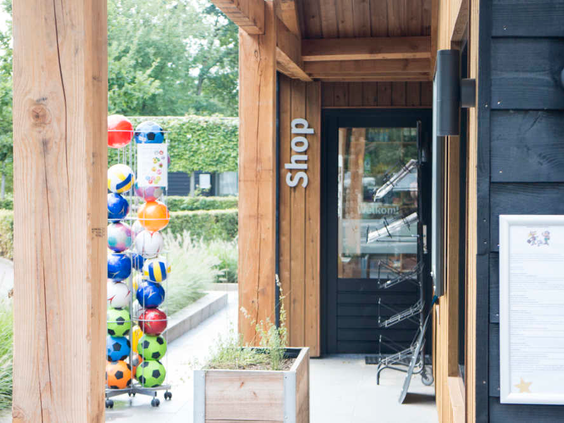 De ingang van de parkwinkel (Shop) van De Wije Werelt, met een rek vol kleurrijke ballen en buitenspeelgoed te koop.