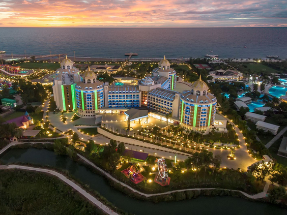 Het prachtig verlichte Delphin BE GRAND Resort in Lara bij zonsondergang, gezien vanuit de lucht.