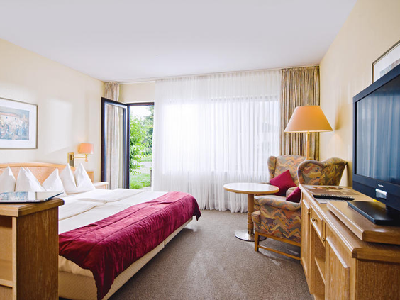 De comfortabele slaapkamer in een van de vakantiehuizen van Dorint Vakantiepark Daun, met een opgemaakt bed en een zithoek.