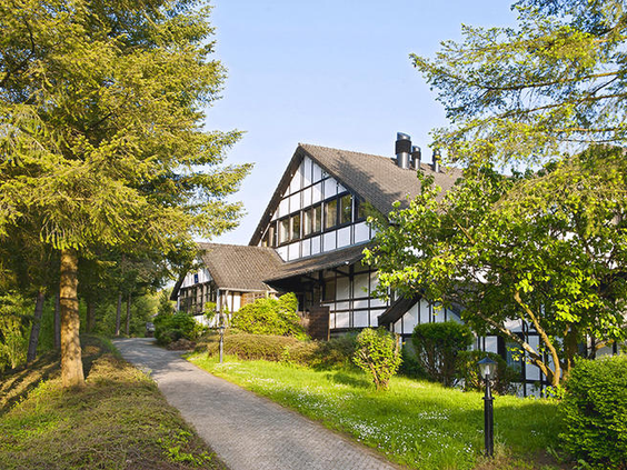 Een sfeervol vakantiehuis in vakwerkstijl op Dorint Vakantiepark Daun, omgeven door de groene natuur en bomen van de Eifel.