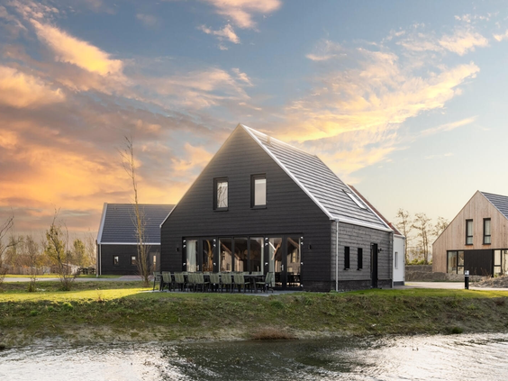 Een luxe, moderne, zwarte vakantiewoning aan het water op Dormio Resort Nieuwvliet-Bad in Zeeland, tijdens een kleurrijke zonsondergang.