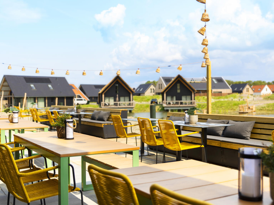 Het zonnige terras van restaurant Ninety aan het water, met uitzicht op de vakantiehuisjes van Dormio Resort Nieuwvliet-Bad.