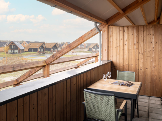 Een overdekt houten balkon van een vakantiewoning op Dormio Resort Nieuwvliet-Bad, met een zitje en uitzicht over het park.