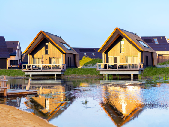 Twee luxe waterwoningen met een houten vlonderterras direct aan het water, weerspiegeld in het water op Dormio Resort Nieuwvliet-Bad.
