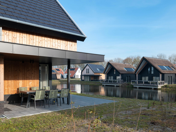 Een ruim, overdekt terras met een grote eettafel direct aan het water bij een moderne vakantiewoning op Dormio Resort Nieuwvliet-Bad.