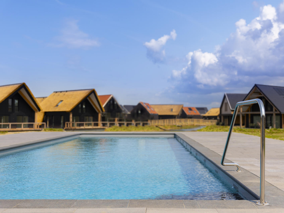 Het verwarmde buitenzwembad van Dormio Resort Nieuwvliet-Bad, omringd door luxe vakantiewoningen onder een helderblauwe lucht.