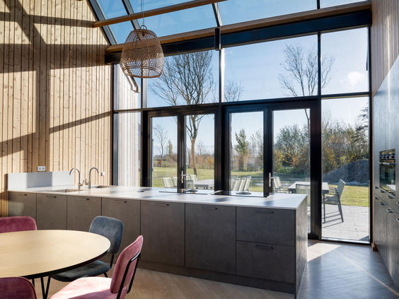 Luxe, lichte keuken in een vakantiewoning op Dormio Resort Nieuwvliet-Bad met een hoog glazen dak en pui, die uitkijkt op de tuin.