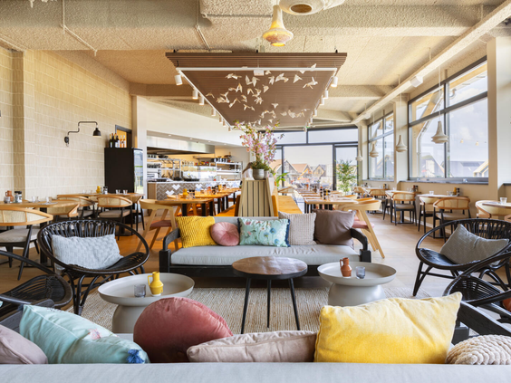 Het sfeervolle lounge-gedeelte van restaurant Ninety op Dormio Resort Nieuwvliet-Bad, met comfortabele banken en kleurrijke kussens.
