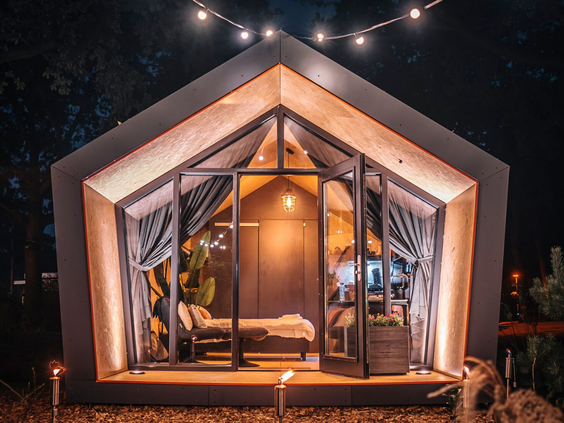 Unieke en luxe glamping accommodatie op Droompark De Zanding, 's nachts verlicht, met een glazen voorkant die uitzicht biedt op de sterrenhemel.