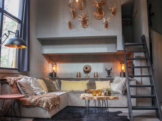 Stoer ingerichte woonkamer in een vakantiehuis op Droompark De Zanding, met een comfortabele loungebank en decoratieve hertengeweien aan de muur.
