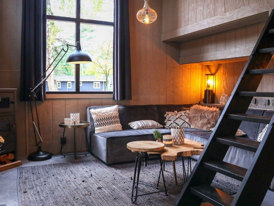 Gezellig ingerichte woonkamer in een houten vakantiehuis op Droompark De Zanding, met een zachte bank en een trap naar de slaapvide.