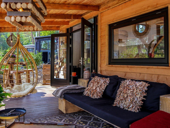 Houten veranda van een vakantiehuis op Droompark De Zanding met een loungebank en een hangstoel, de perfecte plek om te ontspannen.