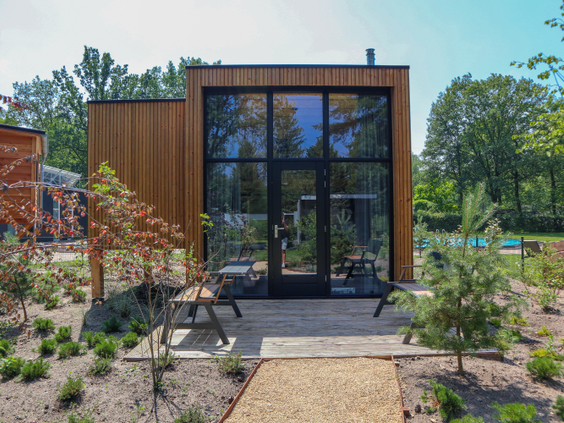 Een moderne, houten vakantiewoning met een grote glazen pui en een terras met een picknicktafel op Droompark Hooge Veluwe.