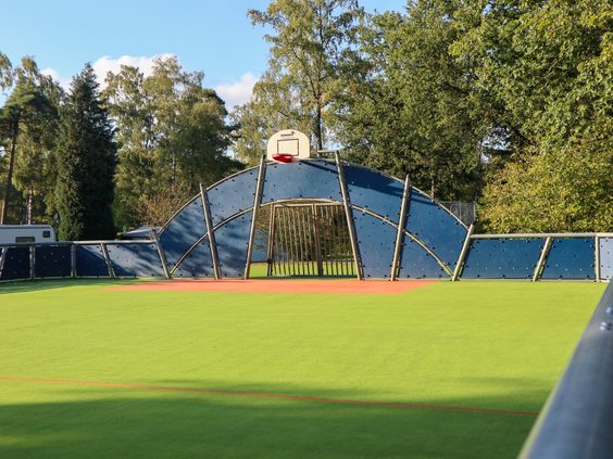 Het omheinde multisportveld op Droompark Hooge Veluwe, met een kunstgrasveld, voetbaldoeltjes en een basketbalnet.
