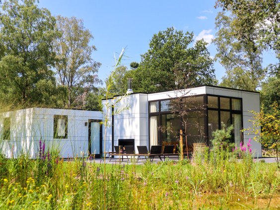 Een moderne, witte design vakantiewoning met een terras, omgeven door wilde bloemen en het groen van de Veluwe op Droompark Hooge Veluwe.