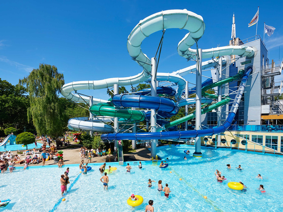 Het buitengedeelte van het Tikibad op Duinrell, met een groot complex van witte en groene waterglijbanen en een vol zwembad op een zonnige dag.