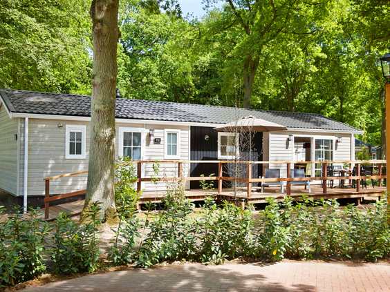 Een luxe Duingalow stacaravan op Vakantiepark Duinrell, met een houten veranda en omgeven door bomen en struiken.