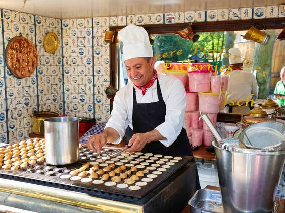 Een vrolijke kok in kokskleding bakt verse poffertjes op een grote bakplaat in een Oudhollandse poffertjeskraam op Duinrell.