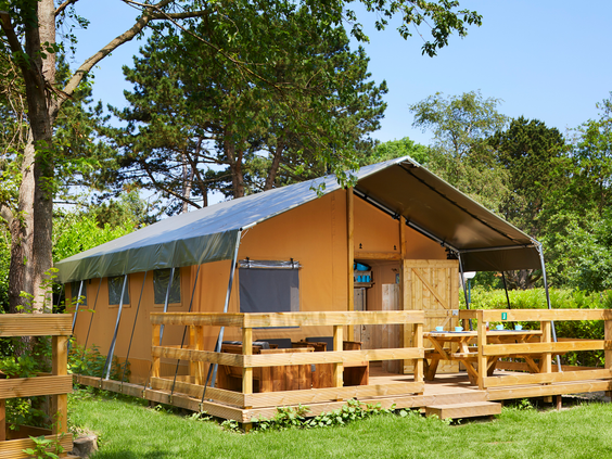 Een luxe lodgetent met een houten veranda, gelegen in het gras op het bosrijke vakantiepark van Duinrell.