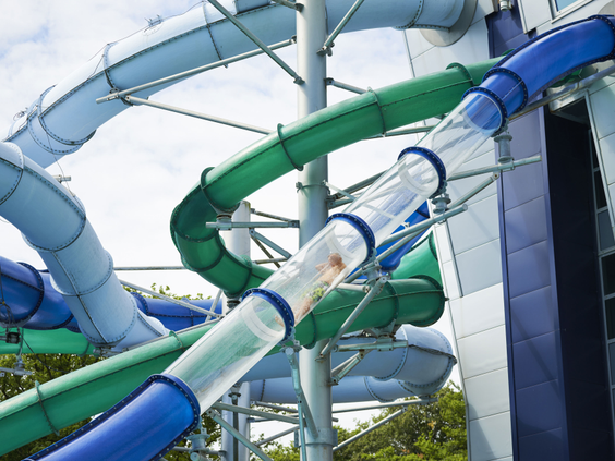 Een wirwar van waterglijbanen in het Tikibad, inclusief een doorzichtige buis met daglichteffecten waar een persoon doorheen glijdt.