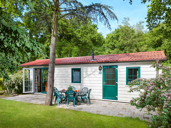 Een witte budget Duingalow op Vakantiepark Duinrell, met een terras met zitje op een grasveld, omgeven door de groene natuur.