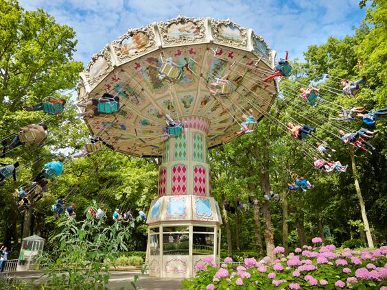 De klassieke zweefmolen de Aqua Swing in Attractiepark Duinrell, omgeven door bomen en bloeiende roze bloemen, met de stoeltjes die door de lucht vliegen.