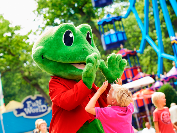 De groene mascotte Rick de Kikker geeft een high-five aan een klein meisje in een roze shirt in het attractiepark van Duinrell.