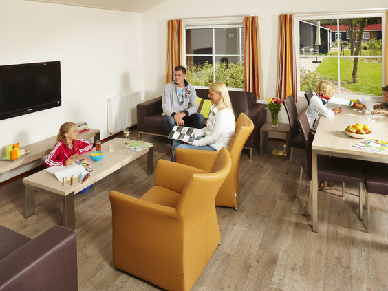 Het interieur van de woonkamer van een Duingalow, waar een gezin ontspant met spelletjes aan de tafel en op de bank zit.