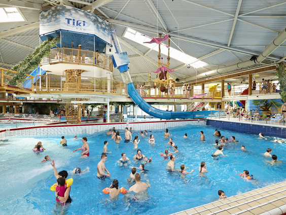 Overzicht van het drukke golfslagbad binnen in het Tikibad, waar veel gezinnen en kinderen genieten van de golven en het zwemmen.