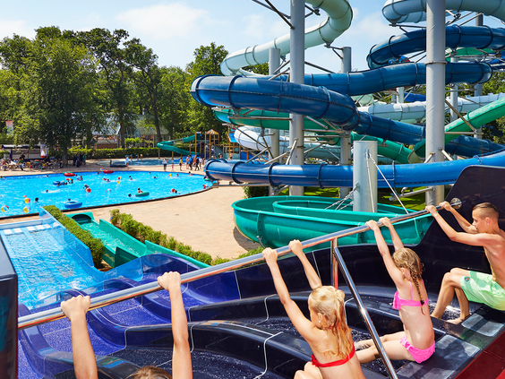 Kinderen houden zich vast aan een stang terwijl ze wachten om met hun band van een van de vele waterglijbanen van het Tikibad af te glijden.