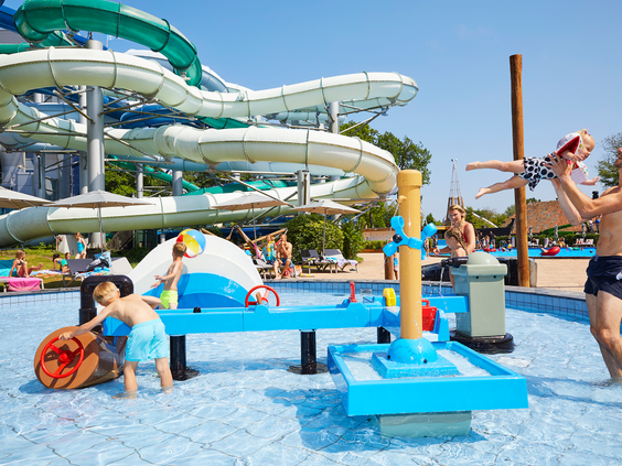 Kinderen spelen in de waterspeeltuin Playa in het Tikibad, met waterspuiters en een klein jongetje dat door zijn vader in de lucht wordt gegooid.