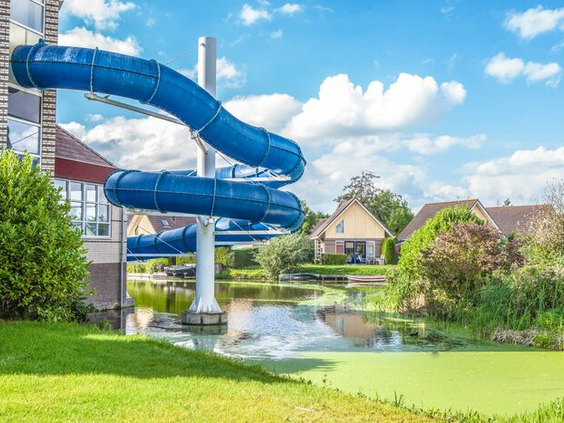 Blauwe waterglijbaan naast een gebouw aan een vijver met vakantiehuisjes bij BungalowSpecials