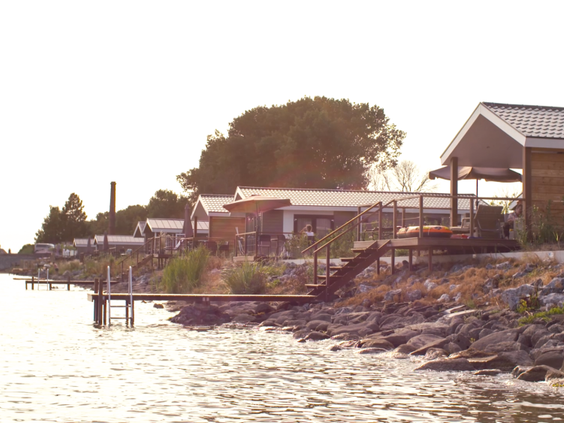 Vakantiehuizen aan de waterkant van EuroParcs Markermeer in Noord-Holland, met de zon die over het water schijnt.