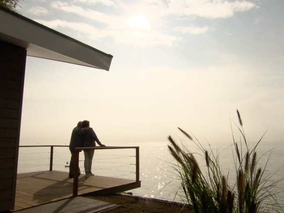 Silhouet van een stel dat vanaf het terras van hun vakantiehuis uitkijkt over het glinsterende water van het Markermeer tijdens zonsondergang.