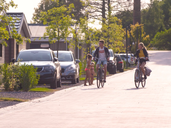 Een gezin fietst vrolijk door de straten van vakantiepark EuroParcs Markermeer, met jonge boompjes langs de weg.