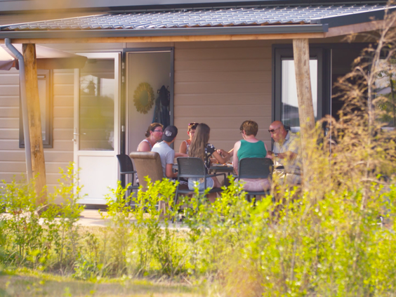 Een groep mensen geniet van het zonnetje op het terras van hun vakantiewoning op EuroParcs Markermeer.