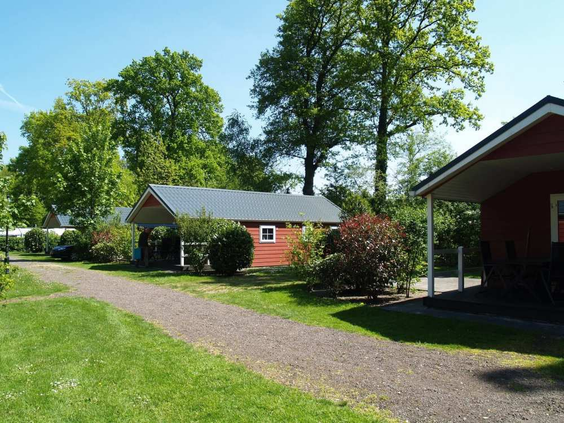 Een rood vakantiehuisje op een rustig pad omgeven door gras en bomen op EuroParcs Resort De Utrechtse Heuvelrug.