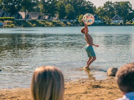 Kind speelt met een bal in het water van de recreatieplas op EuroParcs Resort Limburg, met een zandstrand op de voorgrond.