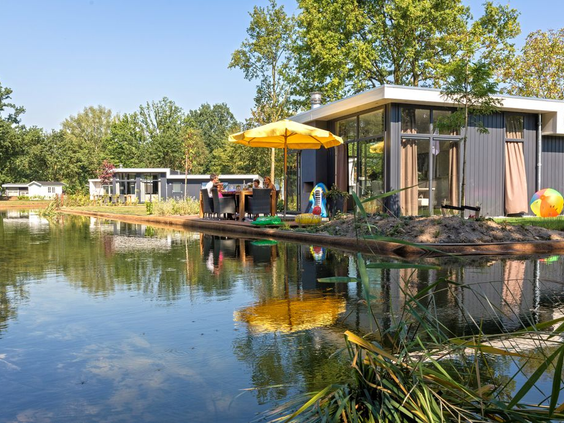 Moderne vakantiewoning met een vlonderterras en gele parasol, direct gelegen aan het water op EuroParcs Resort Limburg.