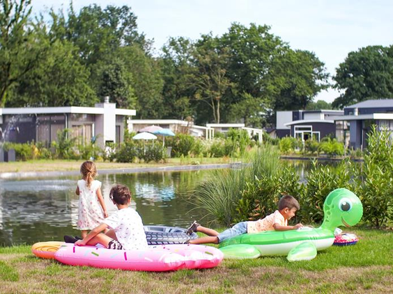 Kinderen spelen met opblaasbare krokodil en luchtbed in het gras aan de rand van het water op EuroParcs Resort Limburg.