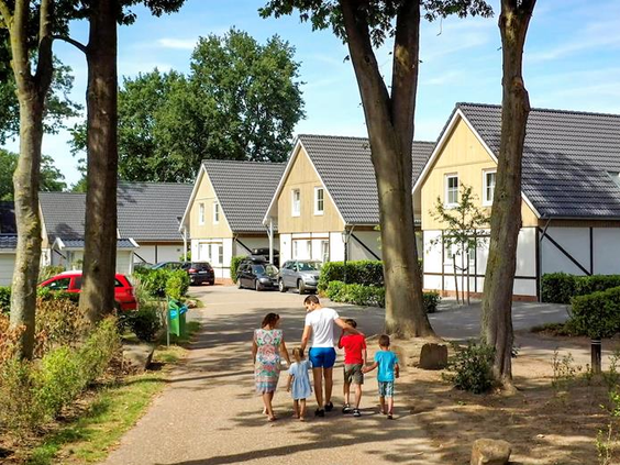 Een gezin wandelt over een pad tussen de bomen op het vakantiepark EuroParcs Resort Limburg, met de vakantiewoningen op de achtergrond.