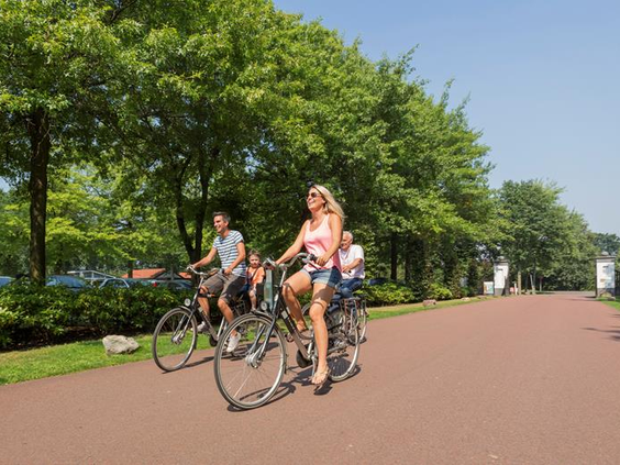 Een familie maakt een fietstocht op een familiefiets en gewone fiets over een fietspad in de groene omgeving van EuroParcs Resort Limburg.