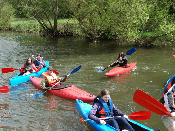Een groep kinderen en volwassenen is aan het kajakken en kanoën op een rivier in de Eifel tijdens hun verblijf in Feriendorf Felsenhof.