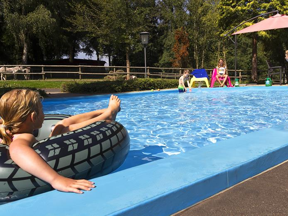 Een meisje relaxt in een grote zwemband in het verkoelende water van het buitenzwembad bij Feriendorf Felsenhof.
