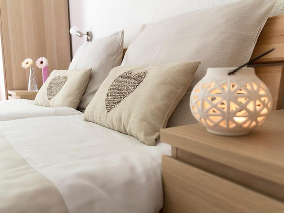 Een sfeervol opgemaakt bed met kussens en een nachtlampje in een van de comfortabele vakantiewoningen van Feriendorf Felsenhof.